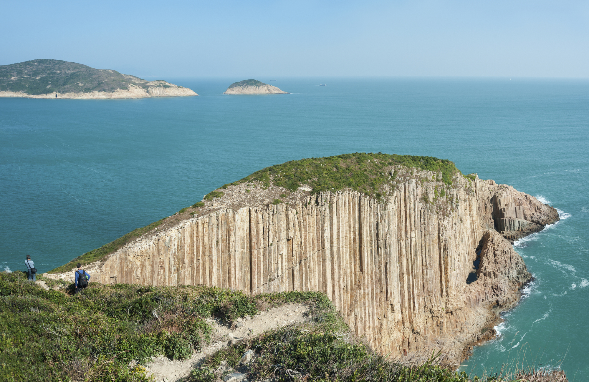 Viewed from a high point, a group of hikers are trekking along a mountain path in Sai Kung, Hong Kong, with continuous mountains and the sea in the distance.